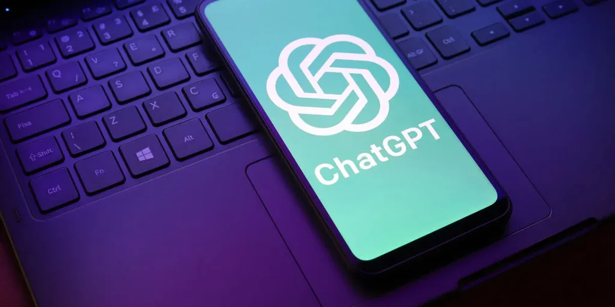Uno smartphone appoggiato sulla tastiera di un laptop mostra sullo schermo il logo e il nome ChatGPT